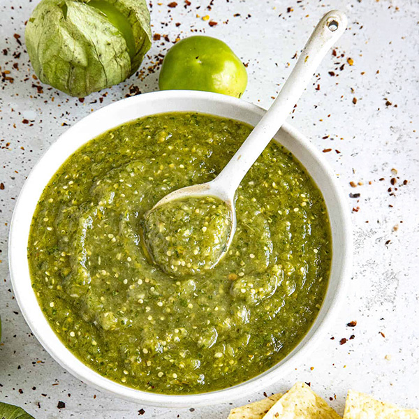 Mexicaanse salsa verde in een kleurrijk aardewerken schaaltje, een tomatillo-gebaseerde saus met koriander, limoen en groene pepers, geserveerd met tortillachips.